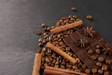 Aromatic set of chocolate bar, arabica coffee beans, anise and cinnamon on dark stone background with copy space