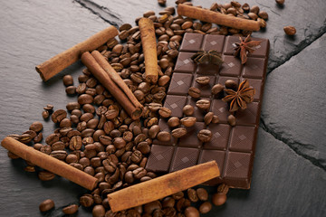 Close-up of roasted arabica coffee beans, dark chocolate bar and spices anise with cinnamon on dark stone background with copy space.
