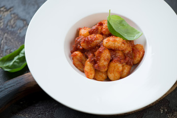 Close-up of a white plate with potato gnocchi served with red pesto sauce, studio shot