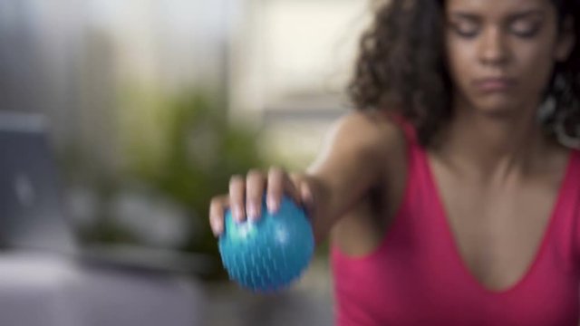 Mixed-race woman squeezing ball in hand, training arms, muscles strength