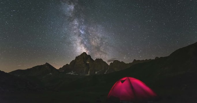 Time Lapse of the Milky way and the starry sky rotating over the majestic Italian French Alps in summertime (M. Viso, 3841 m). Illuminated camping tent in the foreground. Sliding version.