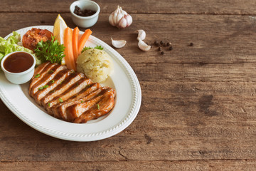 Barbecue pork steak slices on white plate. Delicious pork steak for lunch or dinner on wood table. Moist and soft homemade pork barbecue served with mash potato barbecue sauce and vegetable.