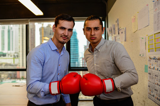 Two businessman look camera with boxing gloves in the office