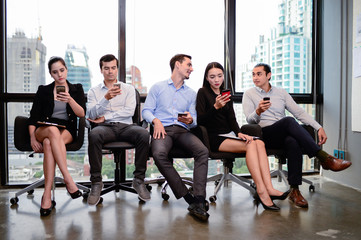 businessman and businesswoman relax sit on chair and write text on smartphone at window in the office