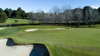 Golf course green with flag, bunkers and tree lined fairways in background
