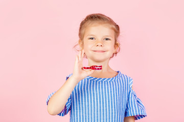 Little beautiful girl in blue stripped shirt is playing red spinner in hand while standing on pink background in studio. Copyspace