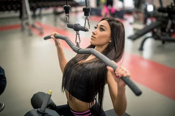 Schilderijen op glas sport, fitness, teamwork and people concept - young woman flexing muscles on gym machine and personal trainer with clipboard © alfa27