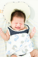 Portrait of a little adorable infant baby girl lying on back on the bed and cry