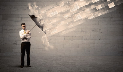Business man protecting with umbrella against wind of papers