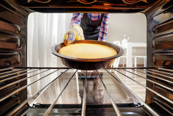 Housewife taking cheesecake out of oven in kitchen
