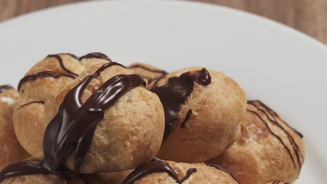 Slow motion fly in shot of profiteroles with fine dark chocolate on plate