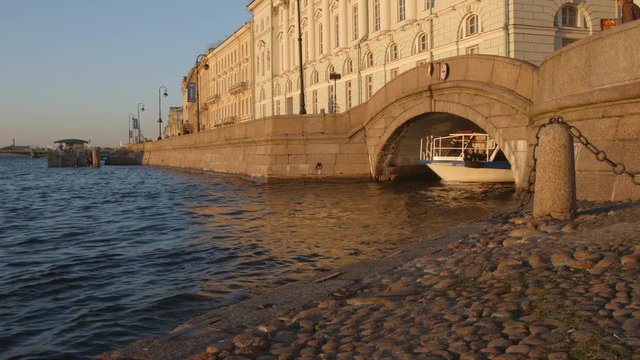 Tour boat moves from the arch of the winter canal into the Neva river in the sunset - St. Petersburg, Russia