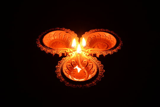 Three lit clay diyas (lamps) placed on a black background.