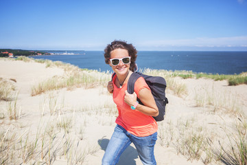 Beautiful young woman traveler with a backpack on the background of the sea and white dunes