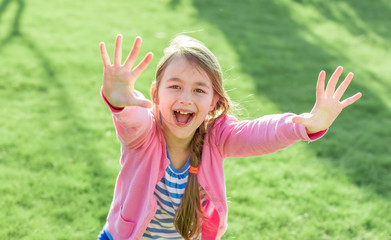 Happy little girl with hands up in summer park.