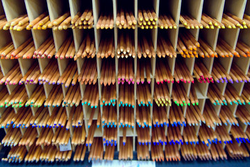 Multicolored pencils in art store in wooden cells closeup, selective focus. Artspace, workshop, creativity concept. Modern art.