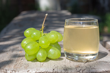 Glass of grape juice and bunch of green grapes on wooden surface