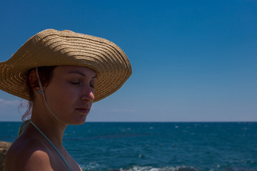 A young girl on the beach, enjoying a holiday in the sun by the sea, a hat on the head, in the background blue sea