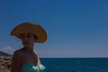 A young girl on the beach, enjoying a holiday in the sun by the sea, a hat on the head, in the background blue sea