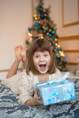 Fototapeta na wymiar ridiculous funny child with gift in front of a Christmas tree, golden background, lifestyle