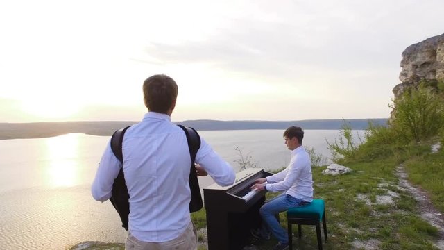 Two musicians Pianist and accordionist playing on the rocks at sunset over sea