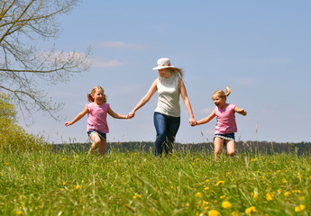 A young mother takes her twin daughters out for a walk  in a flower field. The children enjoy  running and jumping through the