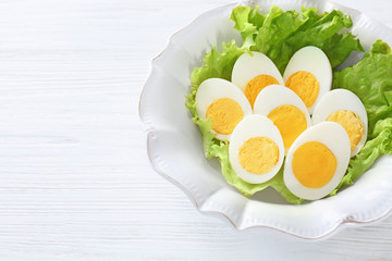 Ceramic plate with sliced hard boiled eggs and lettuce on wooden table. Nutrition concept