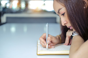 woman sit on her table work, looking sad and writing in a book