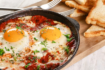 Frying pan with eggs in purgatory on cutting board