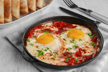 Frying pan with eggs in purgatory on wooden background