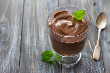 Delicious vegan chocolate mousse with banana, cocoa and mint in glasses on a wooden surface,...