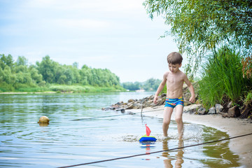 Baby boy playing with ship toy at sea. Child os on vacation in summer at the beach on vacations