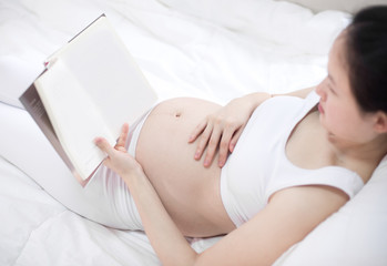 Pregnant Woman Drinking Hot Drink And Reading Book At Home