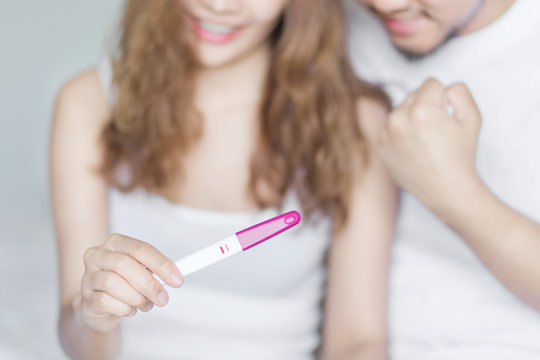 Selective focus happy excited couple for positive pregnancy test in bedroom.