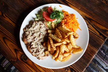 Traditional Latvian rustic dish: pork chop with cream sauce, carrot and cabbage salad, potatoes fries