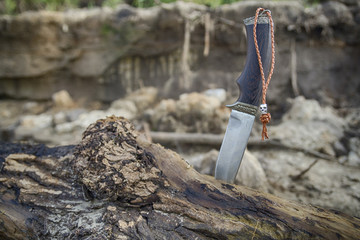 hunting knife with metal skull bead on leather lace stuck in a wooden log, hdr image