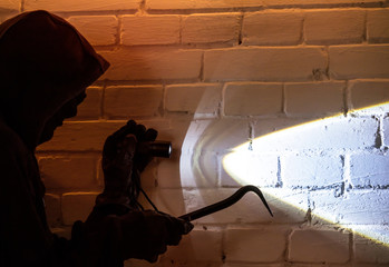 A burglar with tool and lamp penetrates into a house