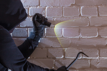 A burglar with tool and lamp penetrates into a house