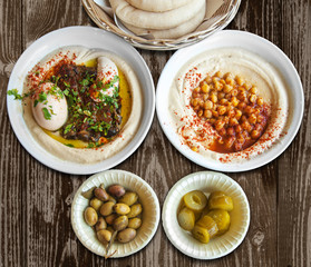 Fresh pita in  wicker bowl, pickled olives, salted cucumbers and hummus  in  white plate on wooden table.
