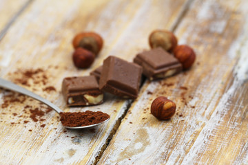 Spoonful of cocoa powder with milk chocolate on rustic wooden surface
