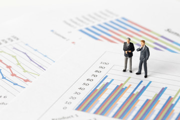 Miniature model of businessman thinking with project for presenting investment concept on graph.