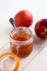 Peach jam in open glass jar with two peaches on white background