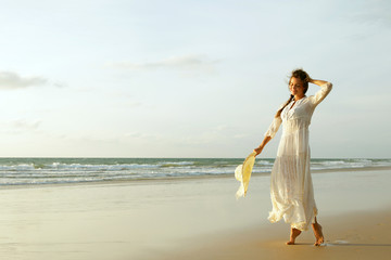 Fototapeta na wymiar Woman wearing beautiful white dress is walking on the beach during sunset