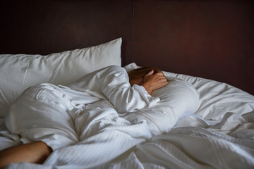 woman laying in bed with white sheets covering head in morning light