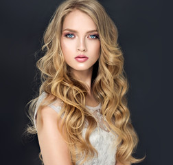 Blonde fashion  girl with long  and   shiny curly hair .  Beautiful  model  in light blue dress with wavy hairstyle .  