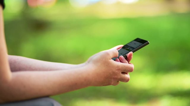 Woman using social networking mobile phone app outdoors in public park accessing web site over open wireless internet