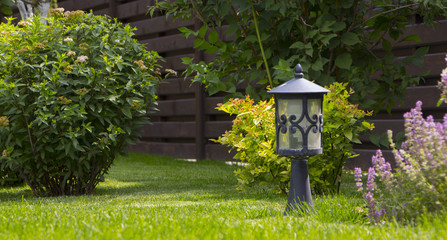 Garden lighting - lights on the solar battery on a green lawn next to a paved path
