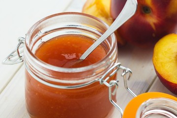 Glass jar of peach and nectarine jam with nectarines on white board