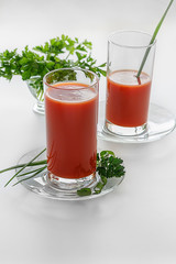 Two glasses of tomato juice and parsley on a white background. The drink red and green onions - a feather and parsley. Life - style. Studio, natural light.