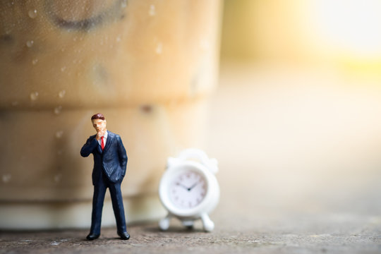 Business, Time And Coffee Concept. Businessman Miniature Figures Standing And Thinking On Wooden Table With A Plastic Cup Of Take Away Iced Coffee And Mini Clock Toy.